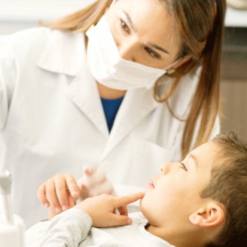 Zahnärztin mit Maske berät Kind auf Behandlungsstuhl